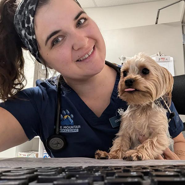 Staff Member Smiling And Holding Puppy At Computer